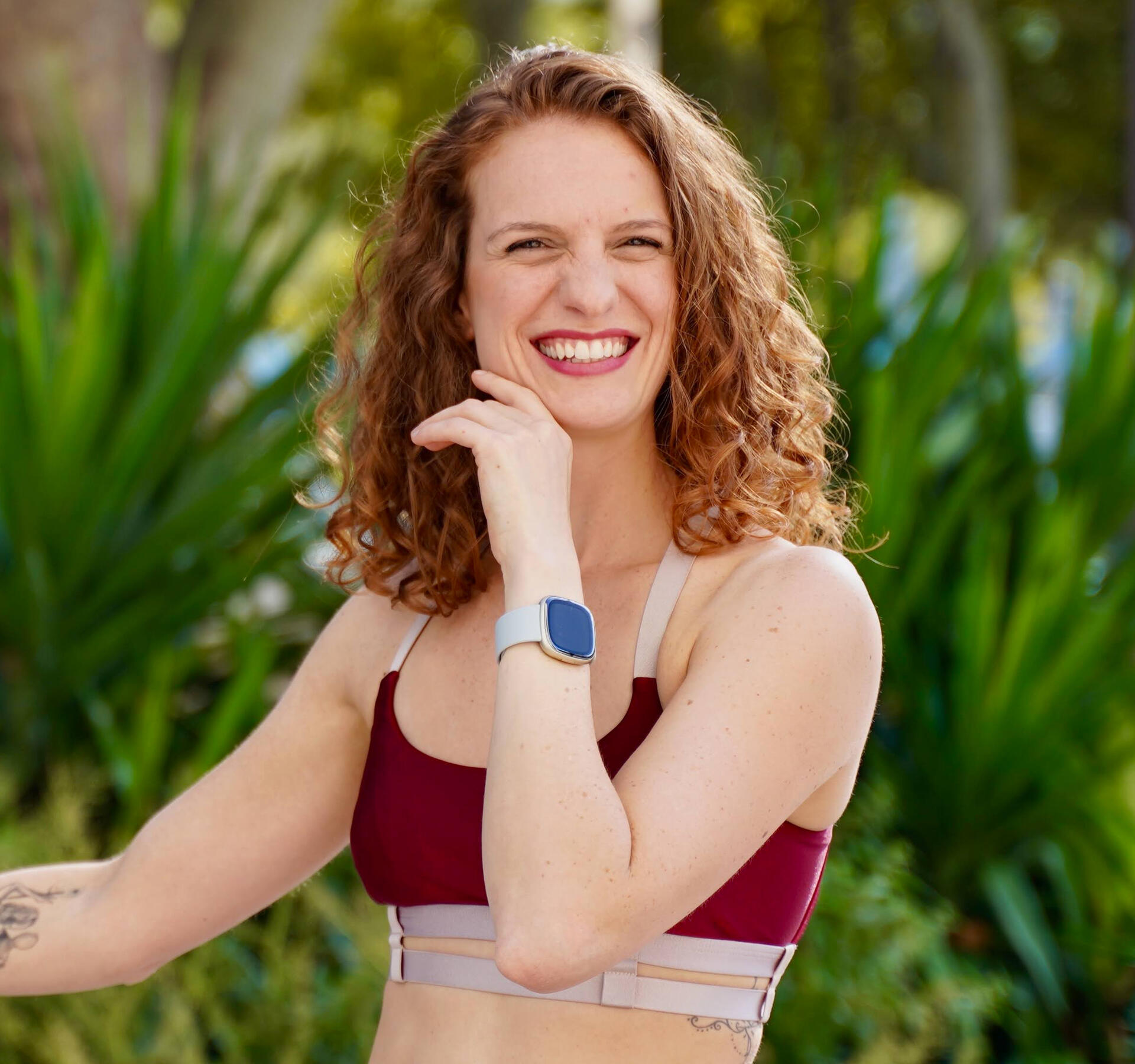 Camila bio picture Camila smiling in a red top and leafy background